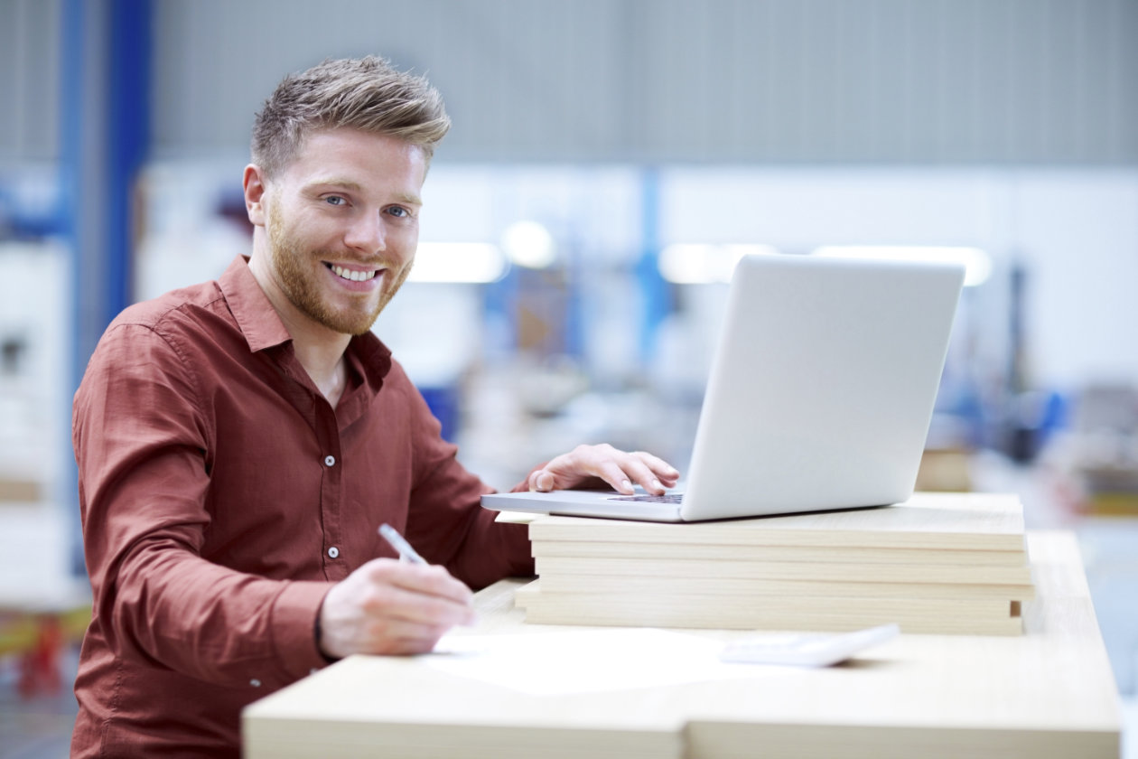 Person an Schreibtisch mit Laptop schaut freundlich in die Kamera